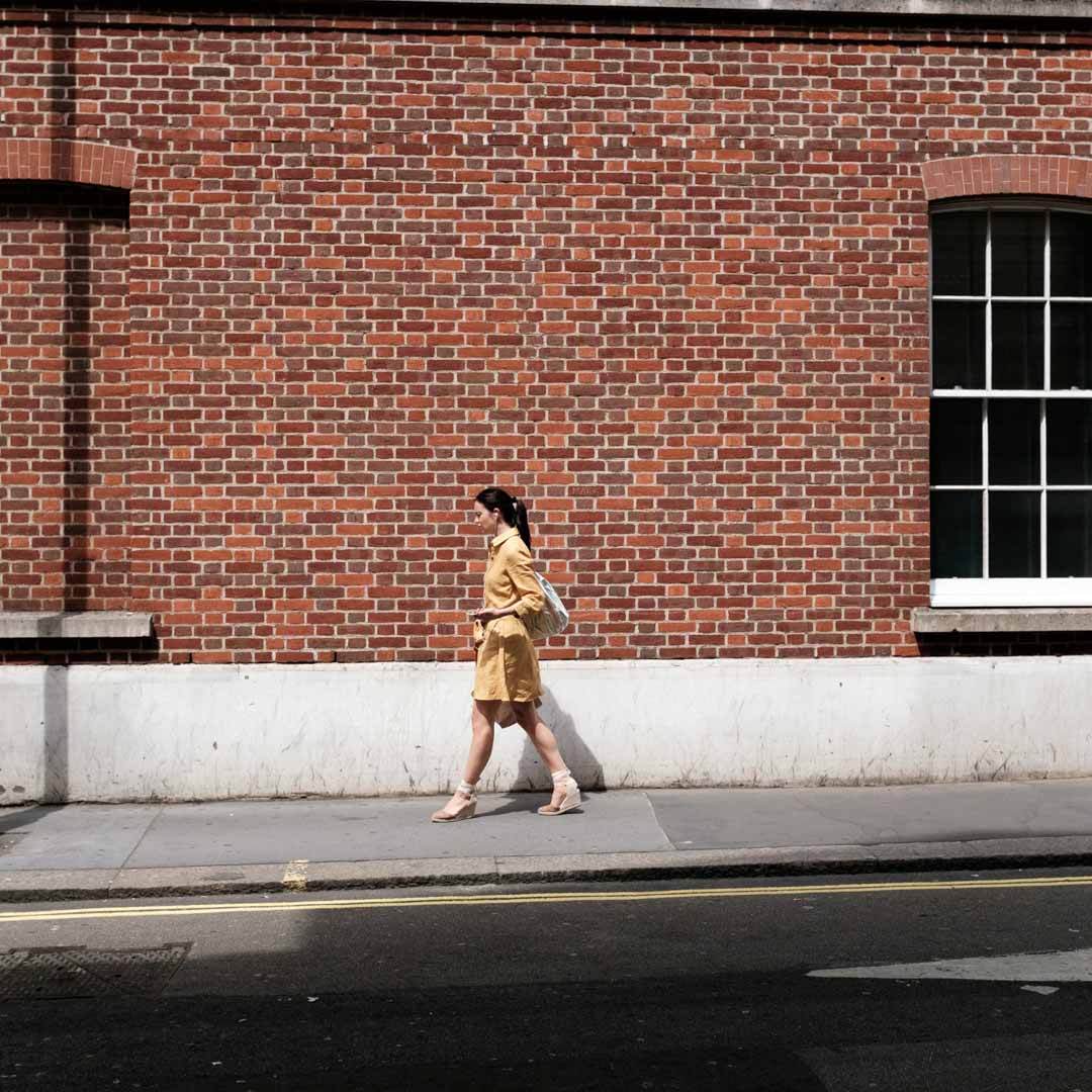 Mujer caminando frente a un muro de ladrillo